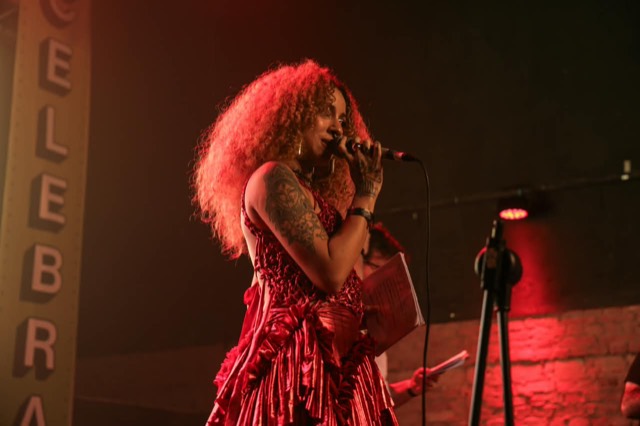 Cantora de vestido vermelho brilhante canta ao microfone no palco.