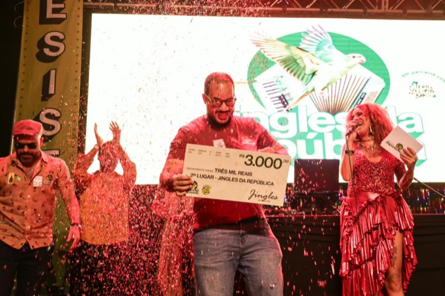 Premiado de camisa vermelha segura o cheque de R$ 3.000 sob uma chuva de confete.