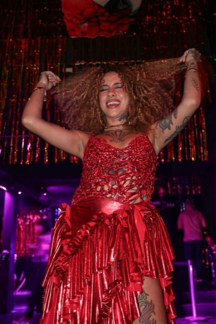 A apresentadora dança na pista, de vestido vermelho.